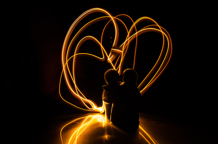 Two young lovers paint a heart on fire. Silhouette of couple and Love words on a dark background. Love conceptの写真素材