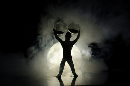Conceptual image with sandglass and and man with moon at background with fog. Silhouette of toy figure touching hourglass. deadline concept. Man rising handsの写真素材