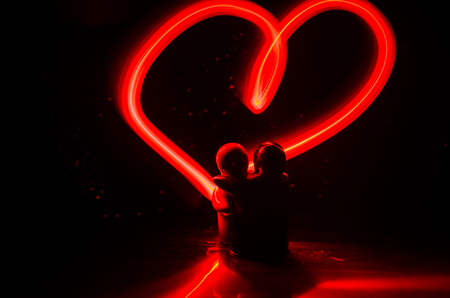 Two young lovers paint a heart on fire. Silhouette of couple and Love words on a dark background. Love conceptの写真素材