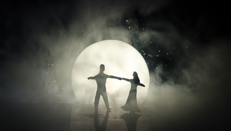 Silhouettes of toy couple dancing under the Moon at night. Figures of man and woman in love dancing at moonlight with fogの写真素材