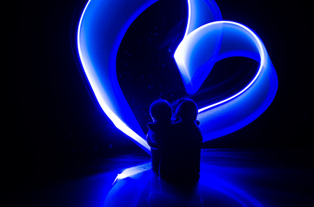 Two young lovers paint a heart on fire. Silhouette of couple and Love words on a dark background. Love conceptの写真素材