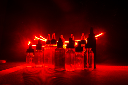 Vape concept. Smoke clouds and vape liquid bottles on dark background. Light effects. Useful as background or vape advertisement or vape background.の写真素材