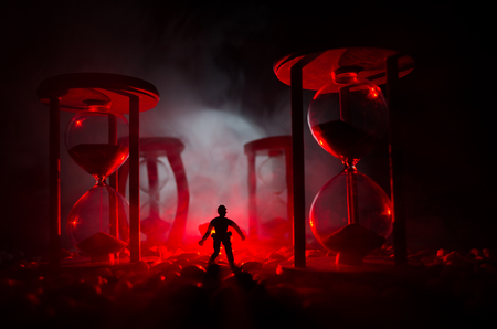 Time concept. Silhouette of a man standing between hourglasses with smoke and lights on a dark...