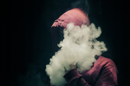 Vaping man holding a mod. A cloud of vapor. Black background. Vaping an electronic cigarette with a lot of smoke. Vape conceptの写真素材