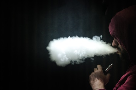 Vaping man holding a mod. A cloud of vapor. Black background. Vaping an electronic cigarette with a lot of smoke. Vape conceptの写真素材