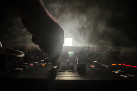 DJ Spinning, Mixing, and Scratching in a Night Club, Hands of dj tweak various track controls on dj's deck, strobe lights and fog, selective focus, close upの写真素材