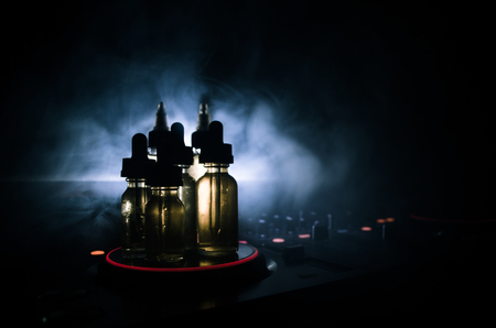 Vape and DJ Club concept. Smoke clouds and vape liquid bottles on Dj mixer close up. Light effects. Useful as background or vape or club advertisementの写真素材