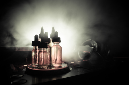 Vape and DJ Club concept. Smoke clouds and vape liquid bottles on Dj mixer close up. Light effects. Useful as background or vape or club advertisementの写真素材