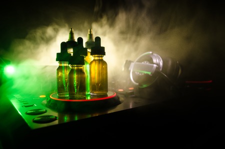 Vape and DJ Club concept. Smoke clouds and vape liquid bottles on Dj mixer close up. Light effects. Useful as background or vape or club advertisementの写真素材