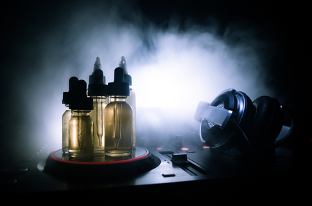 Vape and DJ Club concept. Smoke clouds and vape liquid bottles on Dj mixer close up. Light effects. Useful as background or vape or club advertisementの写真素材