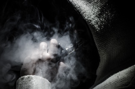 Vaping man holding a mod. A cloud of vapor. Black background. Vaping an electronic cigarette with a lot of smoke. Vape conceptの写真素材