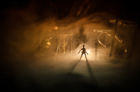 Time concept. Silhouette of a man standing between hourglasses with smoke and lights on a dark background. Surreal decorated pictureの写真素材