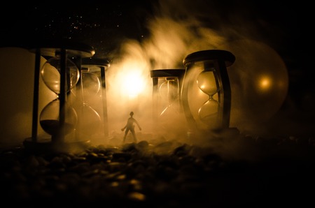 Time concept. Silhouette of a man standing between hourglasses with smoke and lights on a dark background. Surreal decorated pictureの写真素材