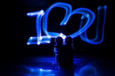 Two young lovers paint a heart on fire. Silhouette of couple and Love words on a dark background. Love conceptの写真素材