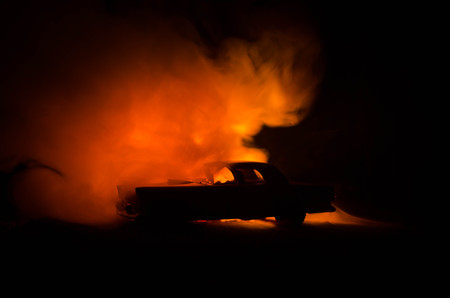 Burning car on a dark background. Car catching fire, after act of vandalism or road indicent. Burning vintage car nightshotの写真素材