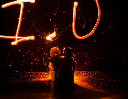 Two young lovers paint a heart on fire. Silhouette of couple and Love words on a dark background. Love conceptの写真素材