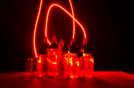 Vape concept. Smoke clouds and vape liquid bottles on dark background. Light effects. Useful as background or vape advertisement or vape background.の写真素材