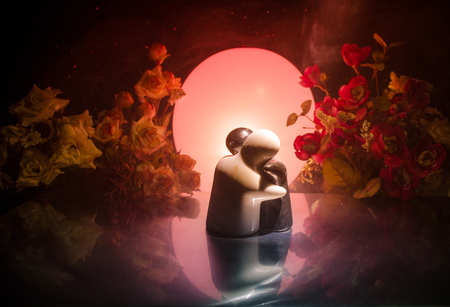 Two doll hugging on table with flowers and moon decoration Lighted background with smoke.Love concept. Greeting or gift card design idea. Silhouette of hugging coupleの写真素材
