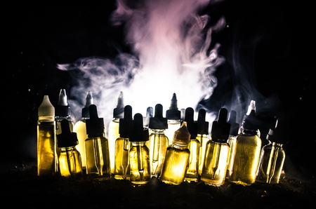 Vape concept. Smoke clouds and vape liquid bottles on dark background. Light effects. Useful as background or vape advertisement or vape background.の写真素材