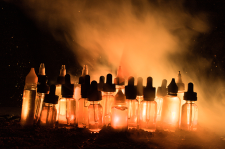 Vape concept. Smoke clouds and vape liquid bottles on dark background. Light effects. Useful as background or vape advertisement or vape background.の写真素材