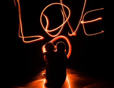 Two young lovers paint a heart on fire. Silhouette of couple and Love words on a dark background. Love conceptの写真素材