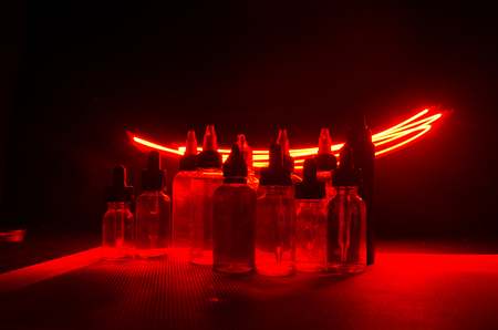 Vape concept. Smoke clouds and vape liquid bottles on dark background. Light effects. Useful as background or vape advertisement or vape background.の写真素材
