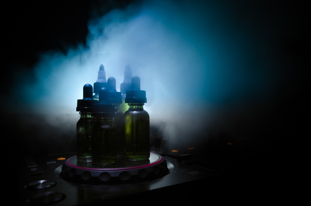 Vape and DJ Club concept. Smoke clouds and vape liquid bottles on Dj mixer close up. Light effects. Useful as background or vape or club advertisementの写真素材