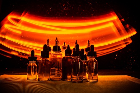 Vape concept. Smoke clouds and vape liquid bottles on dark background. Light effects. Useful as background or vape advertisement or vape background.の写真素材