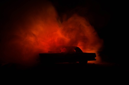 Burning car on a dark background. Car catching fire, after act of vandalism or road indicent. Burning vintage car nightshotの写真素材
