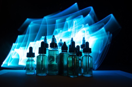 Vape concept. Smoke clouds and vape liquid bottles on dark background. Light effects. Useful as background or vape advertisement or vape background.の写真素材
