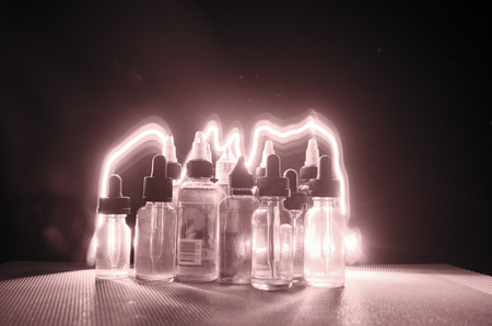 Vape concept. Smoke clouds and vape liquid bottles on dark background. Light effects. Useful as background or vape advertisement or vape background.の写真素材