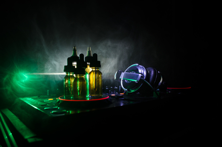 Vape and DJ Club concept. Smoke clouds and vape liquid bottles on Dj mixer close up. Light effects. Useful as background or vape or club advertisementの写真素材