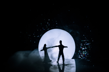 Silhouettes of toy couple dancing under the Moon at night. Figures of man and woman in love dancing at moonlight with fogの写真素材