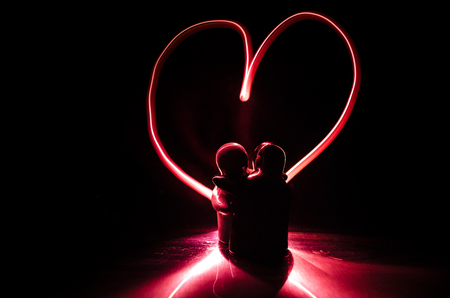 Two young lovers paint a heart on fire. Silhouette of couple and Love words on a dark background. Love conceptの写真素材