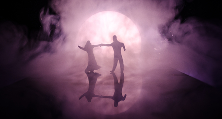 Silhouettes of toy couple dancing under the Moon at night. Figures of man and woman in love dancing at moonlight with fogの写真素材
