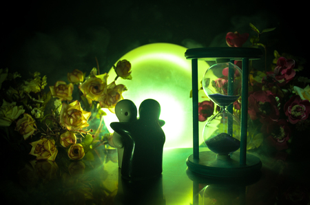 Two doll hugging on table with flowers and moon decoration Lighted background with smoke.Love concept. Greeting or gift card design idea. Silhouette of hugging coupleの写真素材