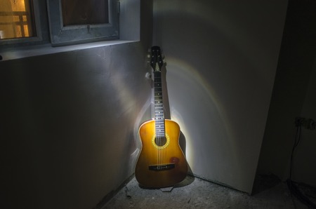 Acoustic guitar leaning on rusty wall in dark room with lights. Surreal view of a room with a guitar. Strobe light on guitarの写真素材
