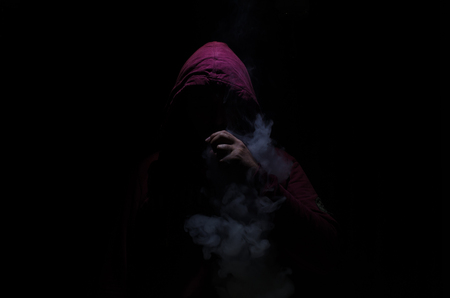 Vaping man holding a mod. A cloud of vapor. Black background. Vaping an electronic cigarette with a lot of smoke. Vape conceptの写真素材