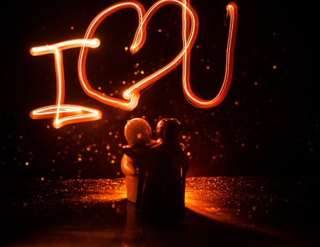 Two young lovers paint a heart on fire. Silhouette of couple and Love words on a dark background. Love conceptの写真素材