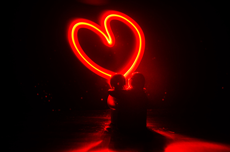 Two young lovers paint a heart on fire. Silhouette of couple and Love words on a dark background. Love conceptの写真素材
