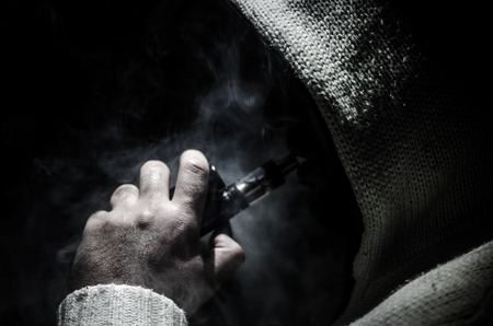 Vaping man holding a mod. A cloud of vapor. Black background. Vaping an electronic cigarette with a lot of smoke. Vape conceptの写真素材