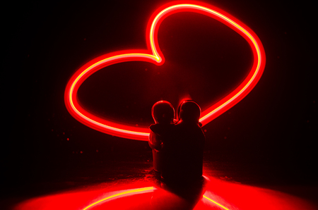 Two young lovers paint a heart on fire. Silhouette of couple and Love words on a dark background. Love conceptの写真素材