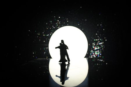 Silhouettes of toy couple dancing under the Moon at night. Figures of man and woman in love dancing at moonlight with fogの写真素材