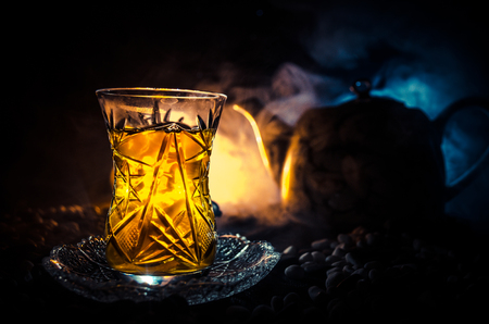 Turkish Azerbaijan tea in traditional glasse and pot on black background with lights and smoke. Eastern tea concept. Armudu traditional cupの写真素材
