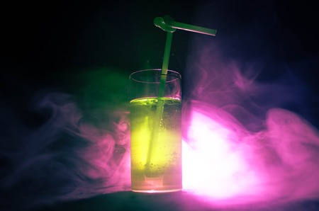 Glass of green cocktail with straw on dark background with smoke and backlights. Colorful coctailの写真素材