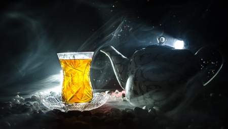 Turkish Azerbaijan tea in traditional glasse and pot on black background with lights and smoke. Eastern tea concept. Armudu traditional cupの写真素材
