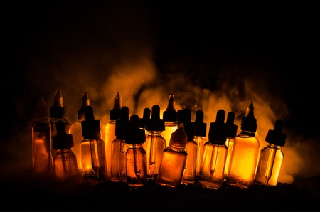 Vape concept. Smoke clouds and vape liquid bottles on dark background. Light effects. Useful as background or vape advertisement or vape background.の写真素材