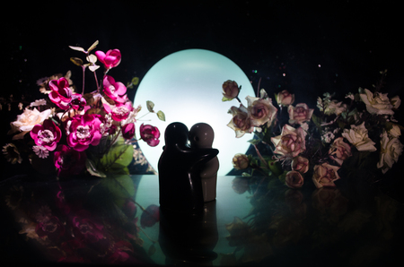 Two doll hugging on table with flowers and moon decoration Lighted background with smoke.Love concept. Greeting or gift card design idea. Silhouette of hugging coupleの写真素材