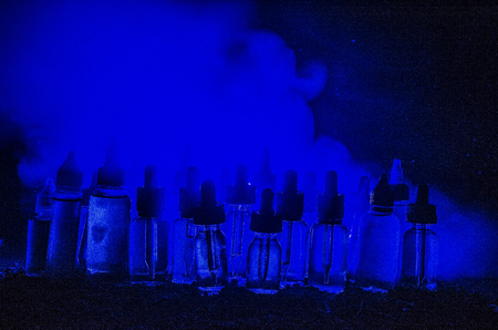 Vape concept. Smoke clouds and vape liquid bottles on dark background. Light effects. Useful as background or vape advertisement or vape background.の写真素材