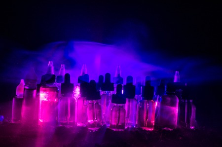 Vape concept. Smoke clouds and vape liquid bottles on dark background. Light effects. Useful as background or vape advertisement or vape background.の写真素材